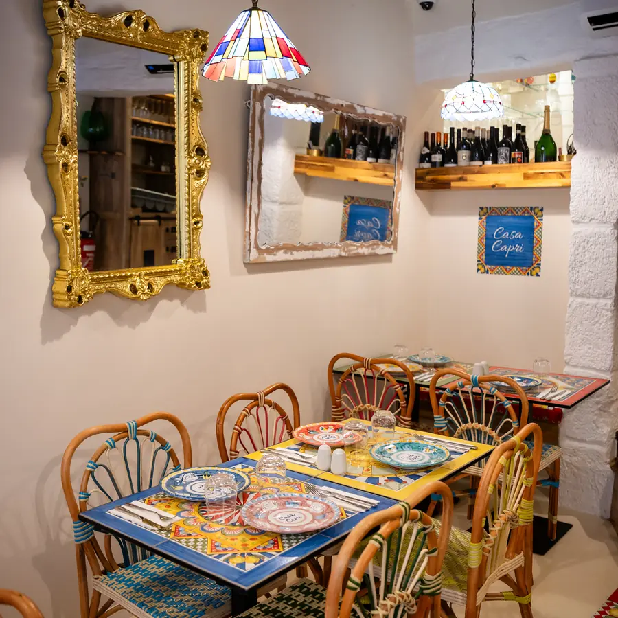 Un coin de la salle, miroir doré et tables dressées sur nappes en faïence.