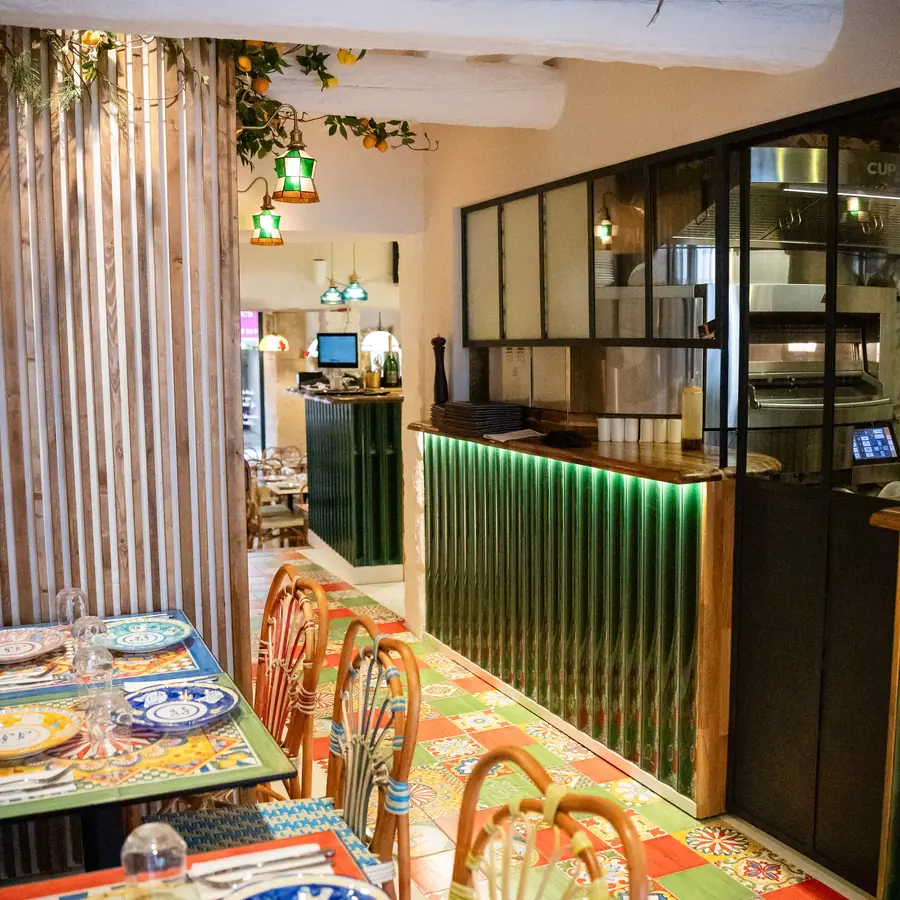 La salle : tables en faïence peinte, chaises en rotin, bar vert et guirlandes de citrons.